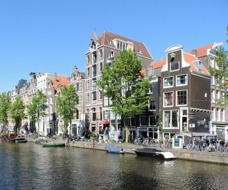 Casas señoriales a lo largo de los canales de Amsterdam con barcos amarrados en un día soleado.